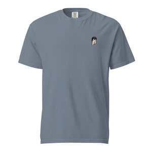 May include: A light blue t-shirt with a small embroidered image of a person's face on the left chest.