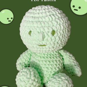 May include: A light green, plush, crocheted Smiski doll with a round head, arms, and legs. The doll has small green eyes and a stitched smile. The text "SMISKI PDF Pattern" is at the top of the image.