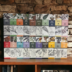 May include: A collection of 24 boxes with various botanical illustrations and Portuguese text. The boxes are arranged in two rows on a wooden shelf. The boxes are white with black text and illustrations.
