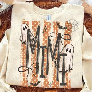 May include: A cream-colored crewneck sweatshirt featuring the text MIMI in large black letters. The design includes two white ghosts, orange vertical stripes with white polka dots, black bows, and small black bats. The Gildan brand tag is visible.