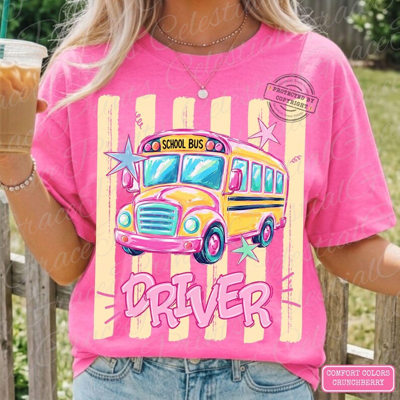 May include: A bright pink t-shirt featuring a graphic of a yellow school bus with the text SCHOOL BUS DRIVER. The design includes light yellow vertical stripes and light blue and green star accents. The shirt has a crew neckline and short sleeves.