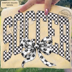 May include: A banana-colored t-shirt with the word "SOCCER" in large, checkered letters. A soccer ball bow is centered below the word. The shirt is held up by a hand.