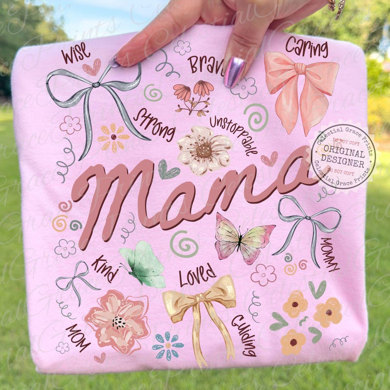 May include: A light pink t-shirt with the word "Mama" in a brown script font. The shirt is decorated with illustrations of bows, flowers, butterflies, and words like "Wise", "Kind", and "Loved".