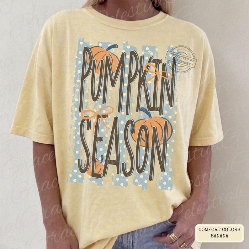 May include: A pale yellow short-sleeve t-shirt featuring a graphic print with the text PUMPKIN SEASON in dark brown letters. The design includes light blue vertical stripes with white polka dots and orange pumpkin illustrations with thin bows.