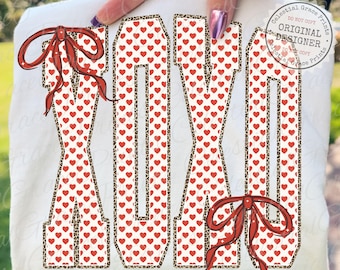 Puede incluir: Camiseta blanca con las letras "XOXO" en estilo universitario. Las letras están rellenas de corazones rojos y delineadas con un estampado de leopardo. Hay lazos rojos en la parte superior e inferior de las letras. También es visible el texto "Celestial Grace Prints".