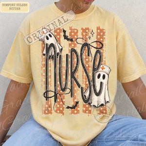 May include: A butter yellow t-shirt featuring a graphic with the word NURSE in large black script. The design includes two white ghosts, one wearing a nurse cap with a red cross, orange vertical stripes with white polka dots, and black bats.