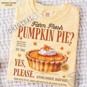 May include: A butter-colored t-shirt featuring a graphic of a pumpkin pie with whipped cream. The text reads: Farm Fresh PUMPKIN PIE? MADE WITH ORGANIC INGREDIENTS, RIGHT HERE, ON OUR FARM EST. 1962 YES, PLEASE. AUTUMN FAVORITE, BAKED DAILY.
