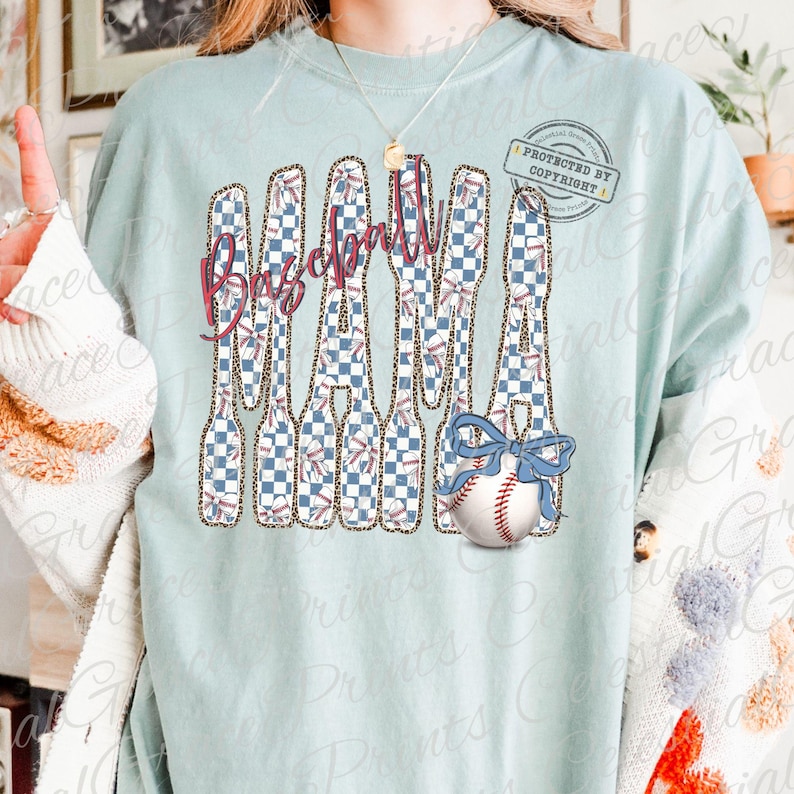 May include: A light blue t-shirt with a baseball-themed graphic. The word "Baseball" is in a script font, with a design of baseball bats and a baseball with a blue bow. The bats have a checkered pattern.