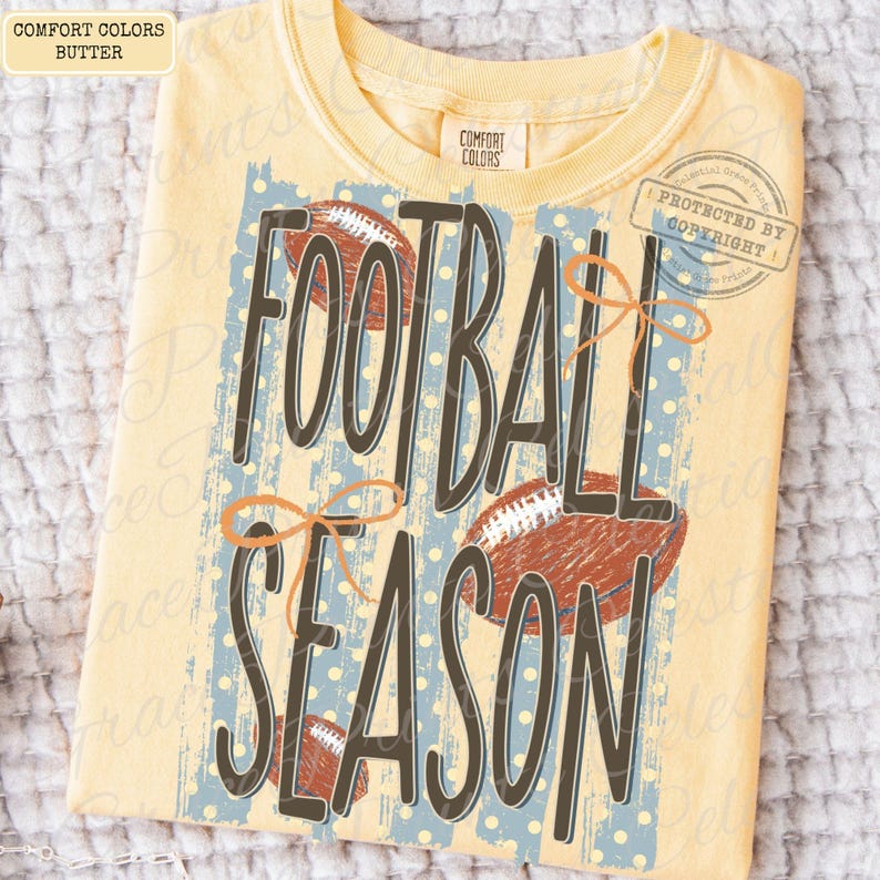 May include: A butter yellow short-sleeve t-shirt featuring a graphic print with the text FOOTBALL SEASON in dark brown letters. The design includes three brown football illustrations, light blue vertical stripes with white dots, and orange bows.