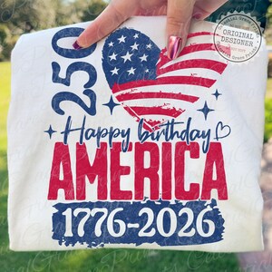 Puede incluir: Camiseta blanca con un dise&ntilde;o patri&oacute;tico. El dise&ntilde;o incluye una bandera americana en forma de coraz&oacute;n, las palabras "Happy birthday AMERICA", los n&uacute;meros "250" y "1776-2026". El dise&ntilde;o es en rojo, blanco y azul.