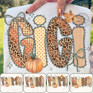 May include: A white t-shirt featuring a graphic print of the word GIGI in large letters with leopard, polka dot, and striped patterns. The design includes a pumpkin, two sage green bows, and an autumn maple leaf, with lace-like borders.