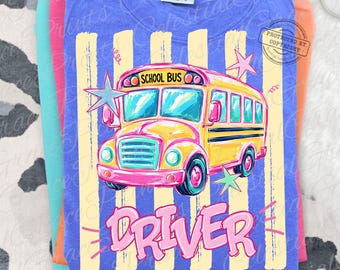 May include: A blue t-shirt featuring a graphic of a yellow school bus with the text SCHOOL BUS above it and the word DRIVER in large pink letters below. The design includes light yellow vertical stripes and several star shapes in the background.