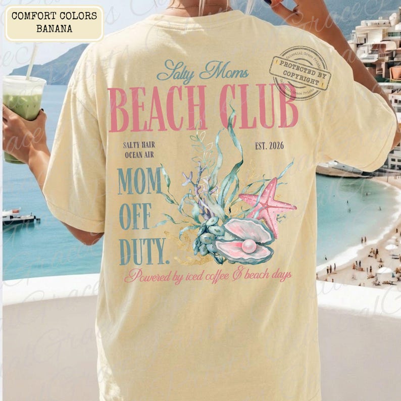 Puede incluir: Camiseta de color pl&aacute;tano con el texto "Salty Moms Beach Club" y un gr&aacute;fico de concha. El dise&ntilde;o incluye una estrella de mar, una perla y las palabras "Mom Off Duty". La camiseta tambi&eacute;n tiene el texto "Powered by iced coffee & beach days."