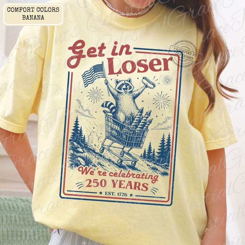 May include: Yellow t-shirt with a graphic featuring a raccoon in a shopping cart, holding an American flag and a hot dog. The text reads "Get in Loser" and "We're celebrating 250 YEARS EST. 1776."