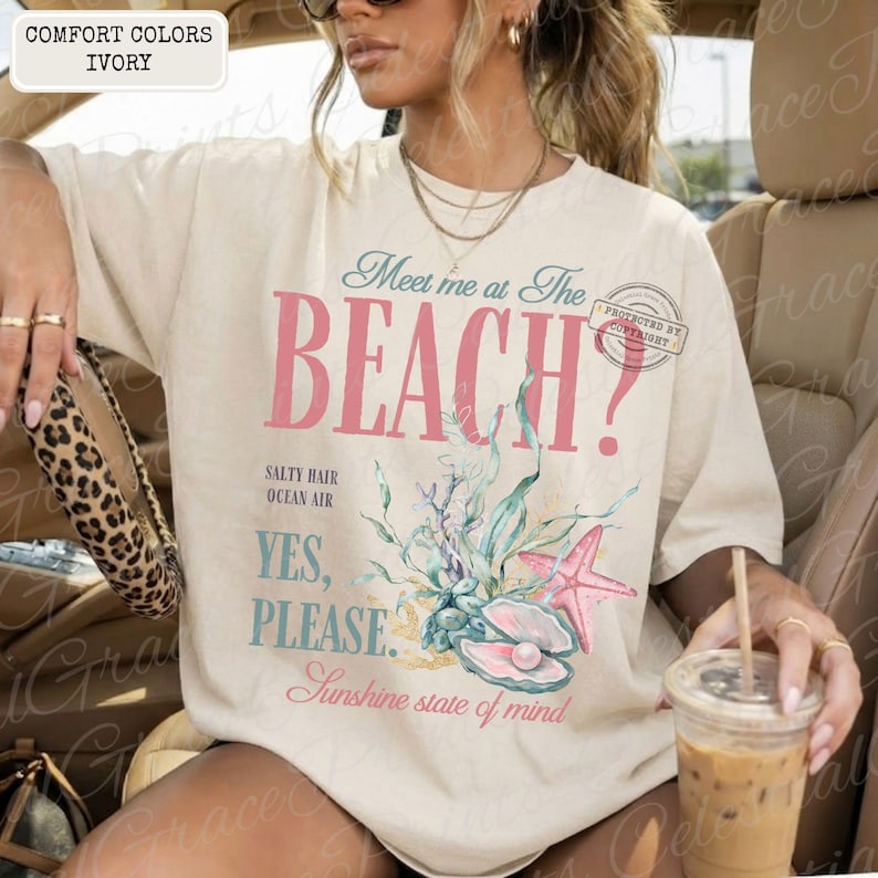 May include: Ivory t-shirt featuring the text "Meet me at The BEACH?" in pink and teal, with a starfish, seashell, and aquatic plants design. The shirt also has the text "YES, PLEASE." and "Sunshine state of mind."