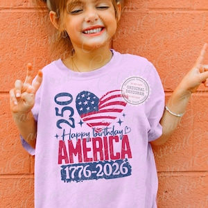 Puede incluir: Una camiseta rosa claro con un dise&ntilde;o patri&oacute;tico. La camiseta presenta una bandera estadounidense en forma de coraz&oacute;n, el texto "Happy Birthday AMERICA 1776-2026" y el n&uacute;mero "250". Un peque&ntilde;o logotipo circular es visible en el lado derecho.