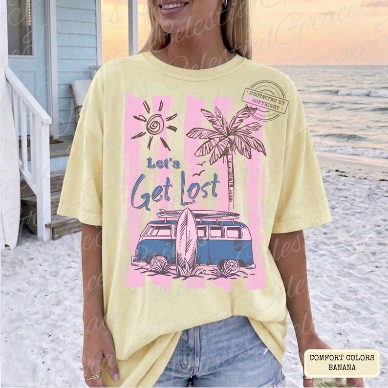 May include: A yellow Comfort Colors t-shirt with a graphic design featuring a sun, palm tree, and a blue van with a surfboard. The text "Let's Get Lost" is displayed in blue script. The shirt is a banana color.