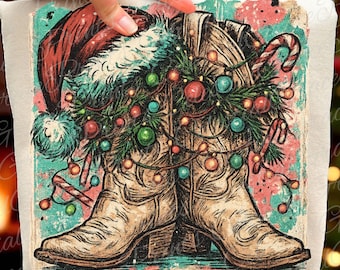 May include: A festive graphic featuring cowboy boots adorned with Christmas lights, ornaments, and candy canes. A Santa hat rests above the boots, creating a holiday theme. The design has a vintage, distressed look with a teal and pink background.
