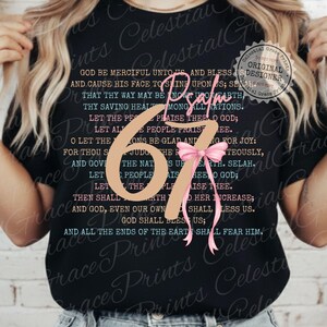 May include: Black t-shirt featuring the text "Psalm 67" with a pink bow and script. The shirt has a religious theme, with a verse printed on the front. The design includes the words "Celestial Grace Prints Designer".
