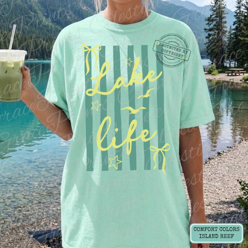 Puede incluir: Camiseta verde claro con la frase "Lake Life" en escritura amarilla, adornada con estrellas, lazos y p&aacute;jaros. El dise&ntilde;o incluye rayas verticales y un sello de copyright. La esquina inferior derecha de la camiseta tiene las palabras "Comfort Colors Island Reef".