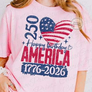Puede incluir: Camiseta rosa claro con un dise&ntilde;o patri&oacute;tico. El dise&ntilde;o incluye una bandera estadounidense en forma de coraz&oacute;n, el texto "Happy Birthday AMERICA", los n&uacute;meros "250" y "1776-2026".