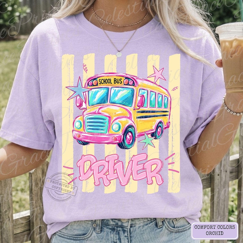 May include: A light purple t-shirt featuring a graphic of a yellow school bus with pink accents and the text "SCHOOL BUS" and "DRIVER" in pink lettering. The design includes light yellow vertical stripes and several light blue and pink stars.
