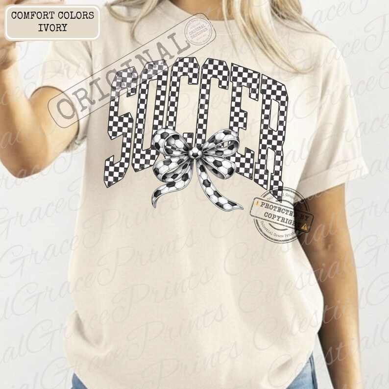 May include: Ivory-colored t-shirt with the word "SOCCER" in a black and white checkered pattern. A bow with soccer ball details is centered below the word. The shirt has short sleeves and a relaxed fit.