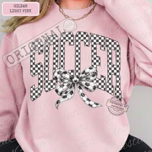 May include: Light pink sweatshirt with the word "SOCCER" in a checkered pattern, with a soccer ball bow. The sweatshirt is a Gildan brand in light pink.