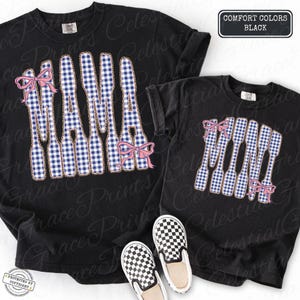 May include: Black t-shirts featuring a "MAMA" design in a blue and white gingham pattern, adorned with pink bows. The shirts are displayed with black and white checkered slip-on shoes. The text "COMFORT COLORS BLACK" is visible.