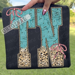 Puede incluir: Sudadera negra con la palabra "PIANO" en turquesa, estampado de leopardo y notas musicales. Lazos rosas acentúan el diseño. La palabra "ORIGINAL" está impresa en la esquina superior izquierda.