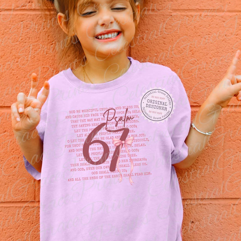 May include: A light pink t-shirt featuring the word "Psalm" and the number "67" in a stylized design. The shirt also includes a passage of text from the Bible. A "Celestial Grace Prints" logo is visible.