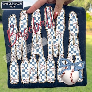 May include: Navy blue t-shirt with the words "Baseball Mama" in a red script font. The letters are filled with a blue and white checkered pattern and baseball-themed designs. A baseball with a blue bow is on the bottom right.
