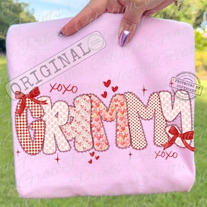 May include: A light pink sweatshirt with the word "Grammy" in a bubble font. The letters are decorated with red and pink hearts and patterns. Red bows and the text "xoxo" are also featured.