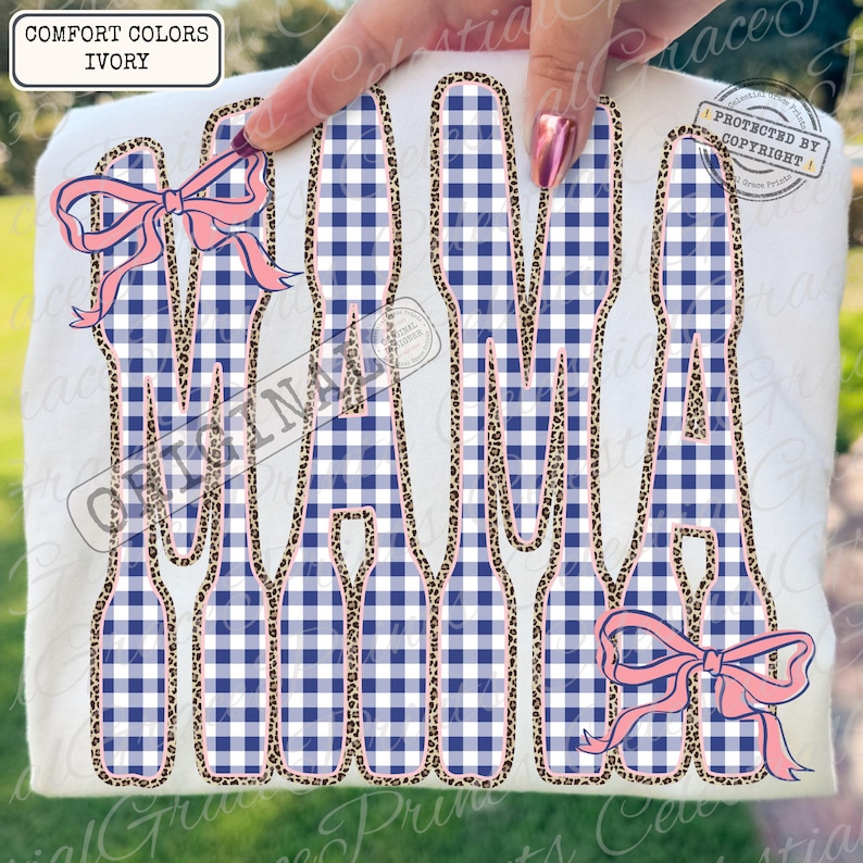 May include: Ivory t-shirt featuring the word "MAMA" in large letters. The letters are filled with a blue and white gingham pattern and outlined with a leopard print. Pink bows are placed on the top and bottom of the word.
