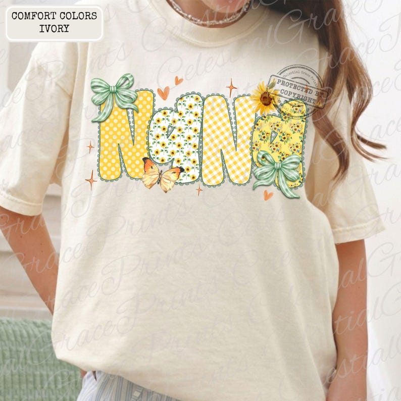 May include: Ivory-colored t-shirt with the word "Nana" in a whimsical design. The letters feature polka dots, sunflowers, and gingham patterns, accented with butterflies, bows, and hearts. The shirt is labeled "Comfort Colors Ivory."