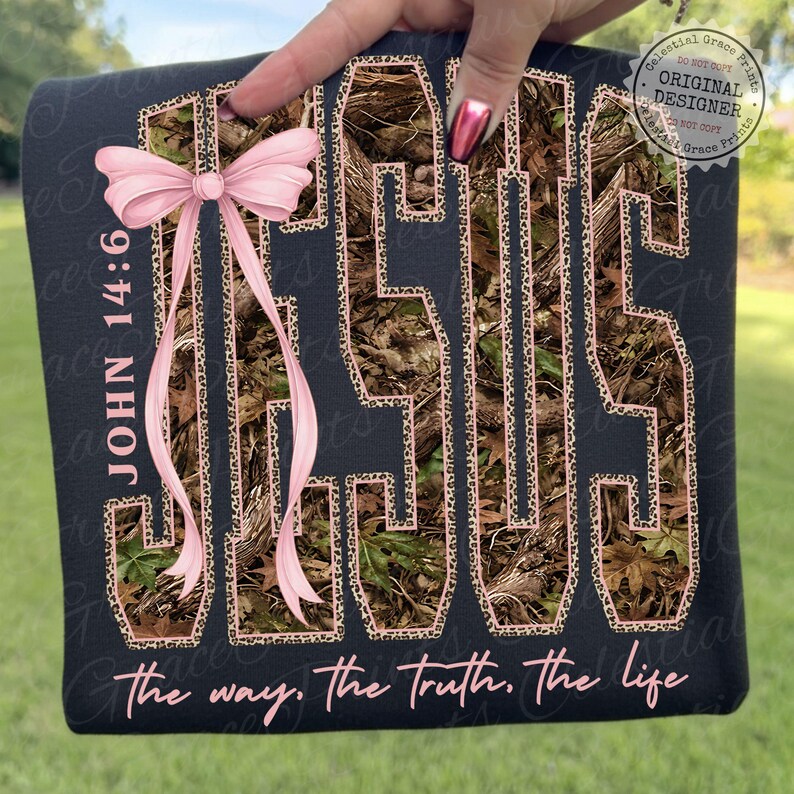 May include: Black fabric with the word "JESUS" in large letters, filled with a camouflage pattern and outlined in leopard print. A pink bow and the text "JOHN 14:6" are on the left. The phrase "the way, the truth, the life" is at the bottom.