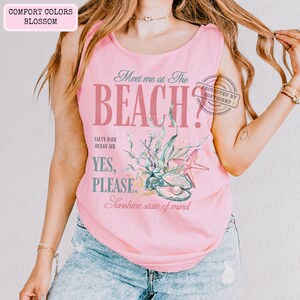 May include: A pale pink vest top featuring the words "Meet me at The BEACH?" in a vintage style. The design incorporates illustrations of seashells, starfish, and seaweed. The text "Salty Hair, Ocean Air, Yes, Please, Sunshine state of mind" is also included.