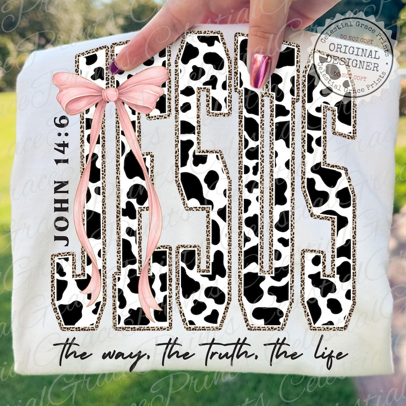 Puede incluir: Camiseta blanca con la palabra "JESUS" en un dise&ntilde;o de estampado de vaca en blanco y negro, delineada con un estampado de leopardo. Un lazo rosa y el texto "JOHN 14:6" est&aacute;n a la izquierda. La frase "the way, the truth, the life" est&aacute; en la parte inferior.