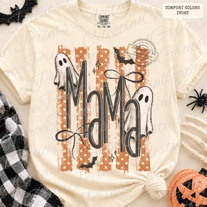 May include: An ivory short-sleeve t-shirt featuring the text MAMA in large black letters. The design includes two white ghosts, black bats, and orange vertical stripes with white polka dots. The shirt has a crew neck and a Comfort Colors label.