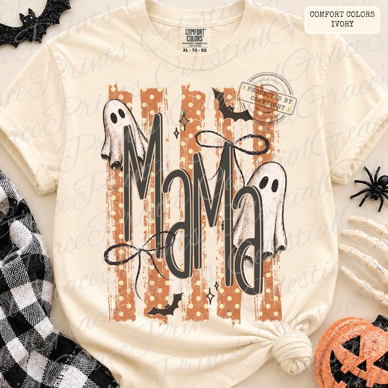 May include: An ivory short-sleeve t-shirt featuring the text MAMA in large black letters. The design includes two white ghosts, black bats, and orange vertical stripes with white polka dots. The shirt has a crew neck and a Comfort Colors label.