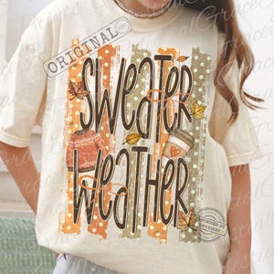 May include: A cream-colored t-shirt featuring a graphic print with the text "SWEATER WEATHER" in dark brown script. The design includes vertical orange and tan stripes with white polka dots, a textured orange sweater, and a coffee cup with autumn leaves.