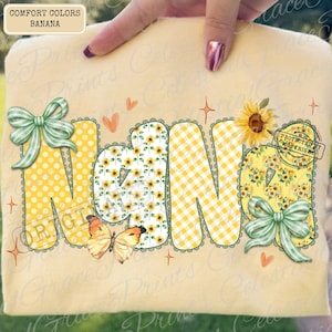 May include: A light yellow t-shirt with the word "NANA" in large, colorful letters. The letters feature polka dots, sunflowers, and gingham patterns. The design includes butterflies, bows, and a sunflower, creating a cheerful, personalized look.