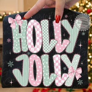 以下が含まれることがあります： 「HOLLY JOLLY」の文字が遊び心のあるフォントで描かれた黒いスウェットシャツ。文字はピンクとグリーンの模様、雪の結晶、リボンで装飾されています。デザインは、お祝いのホリデーテーマです。