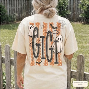 May include: An ivory t-shirt featuring a back graphic with the text GIGI in large black letters. The design includes orange vertical stripes with white polka dots, two white ghost illustrations, small black bats, and stars. The shirt has a crew neck.