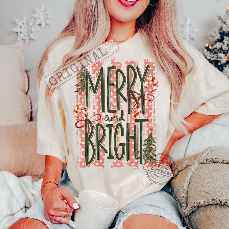 May include: A cream-colored short-sleeve t-shirt featuring a graphic print with vertical red and white stripes. The text reads MERRY and BRIGHT in dark green lettering, accompanied by illustrations of two candy canes and two pine trees.