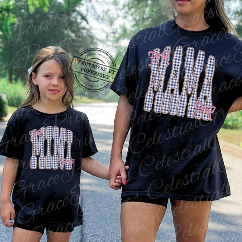 May include: Black t-shirts featuring the words "MAMA" and "MINI" in a blue and white gingham design, adorned with pink bows. A mother and child are seen wearing the matching shirts, holding hands.