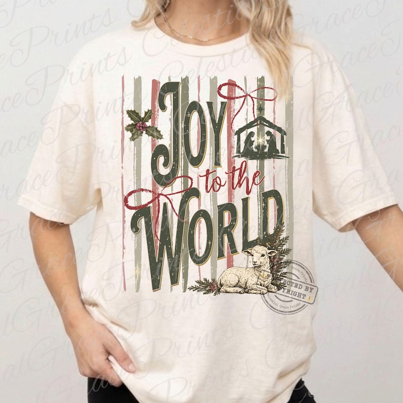 Puede incluir: Una camiseta de manga corta color crema con un gr&aacute;fico de rayas verticales en rojo y verde apagados. El texto Joy to the World aparece en cursiva verde oscuro. El dise&ntilde;o incluye un bel&eacute;n, acebo y la ilustraci&oacute;n de un peque&ntilde;o cordero.