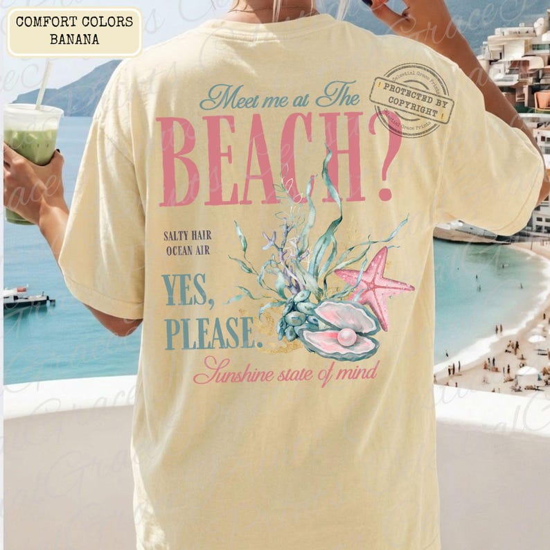 May include: A cream-coloured t-shirt with the words "Meet me at the BEACH?" in pink and blue. The back of the shirt features a seashell, starfish, and aquatic plant graphic. The words "Salty Hair, Ocean Air, Yes, Please, Sunshine state of mind" are also printed.