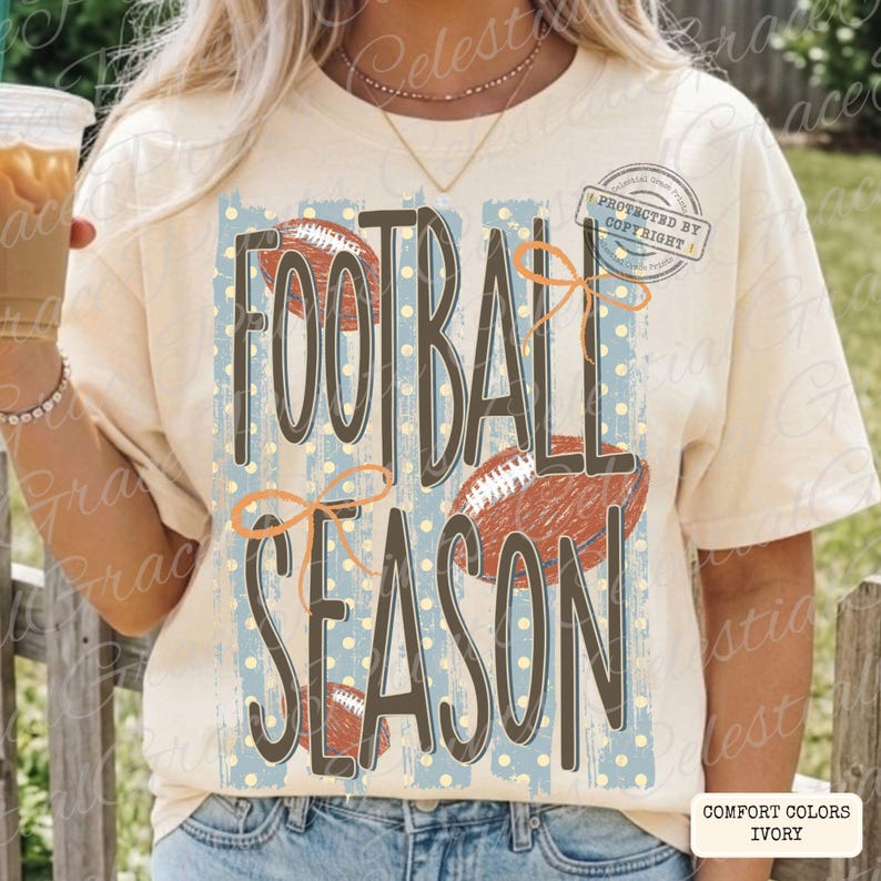 May include: An ivory short-sleeve t-shirt featuring a graphic print with the text FOOTBALL SEASON in dark brown letters. The design includes three brown football illustrations, light blue vertical stripes, and orange line-drawn bows.