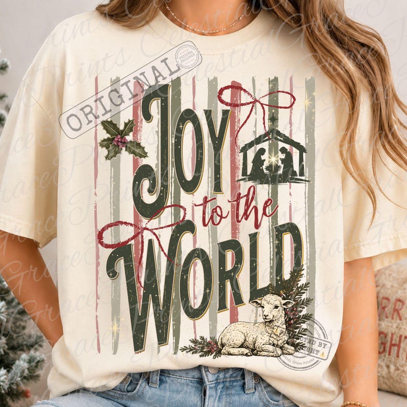 Puede incluir: Una camiseta de color crema con un gr&aacute;fico que incluye el texto Joy to the World en verde oscuro y rojo. El dise&ntilde;o presenta una silueta de bel&eacute;n, un cordero, hojas de acebo y rayas verticales en tonos rojos y verdes apagados.